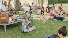 Mehrere Personen sitzen beim Feel Good Festival auf der Wiese und praktizieren Yoga und Meditation gemeinsam
