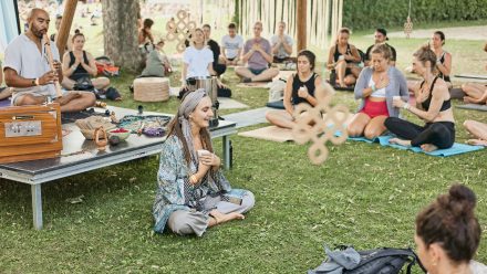 Mehrere Personen sitzen beim Feel Good Festival auf der Wiese und praktizieren Yoga und Meditation gemeinsam