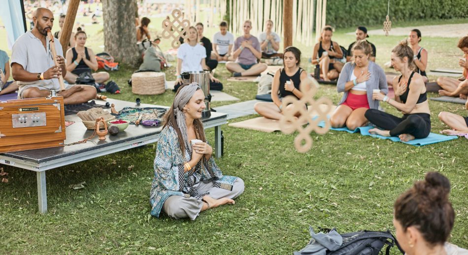 Mehrere Personen sitzen beim Feel Good Festival auf der Wiese und praktizieren Yoga und Meditation gemeinsam